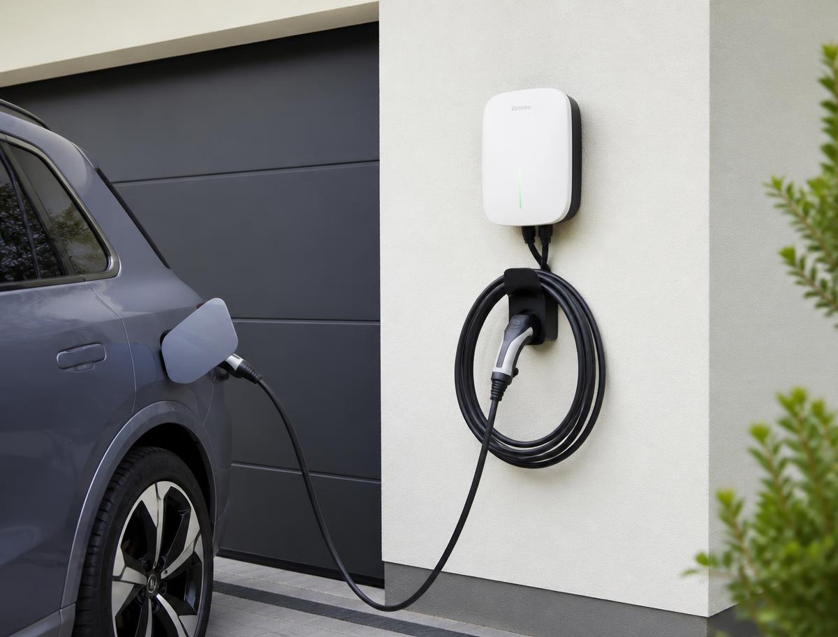 Wallbox an einer Hauswand mit ladendem Elektroauto